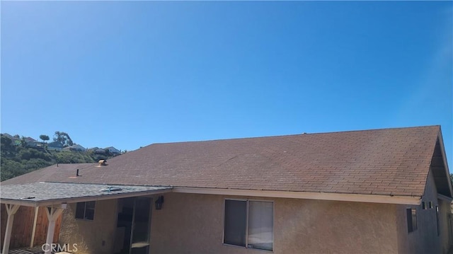 view of side of home featuring stucco siding and a shingled roof