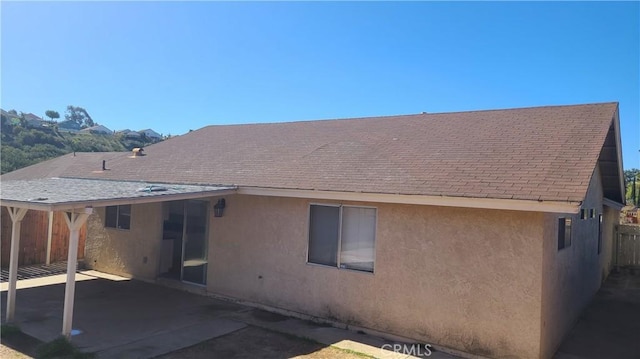 rear view of property featuring stucco siding, a patio area, and a shingled roof