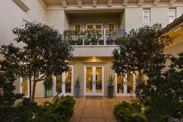 view of exterior entry featuring french doors, a balcony, and stucco siding