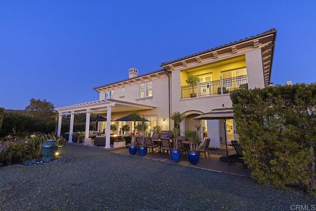 back of house with stucco siding, a chimney, a balcony, a pergola, and a patio