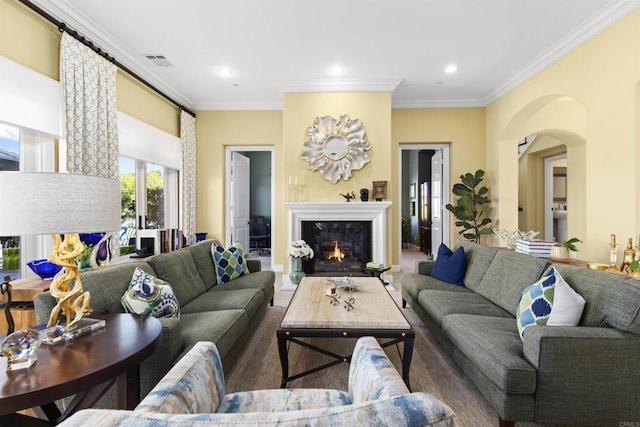 living area featuring wood finished floors, visible vents, recessed lighting, a warm lit fireplace, and ornamental molding