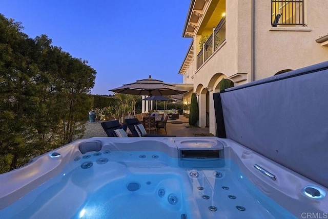 pool at dusk with a hot tub and a patio