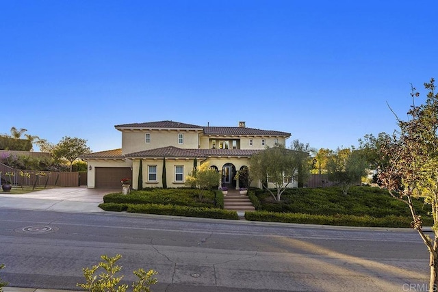 mediterranean / spanish-style house featuring fence, driveway, stucco siding, a garage, and a tiled roof