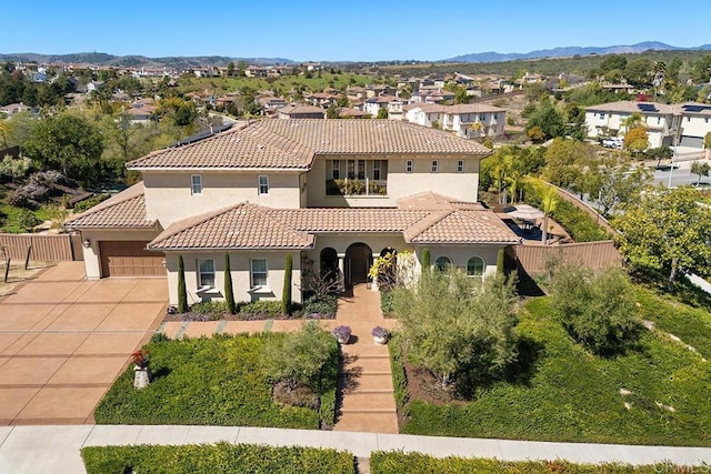 mediterranean / spanish home with a tiled roof, concrete driveway, stucco siding, and fence