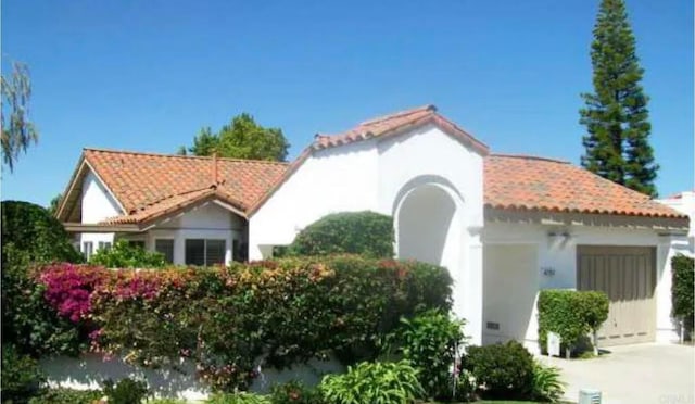 view of front facade featuring stucco siding, a tile roof, and a garage