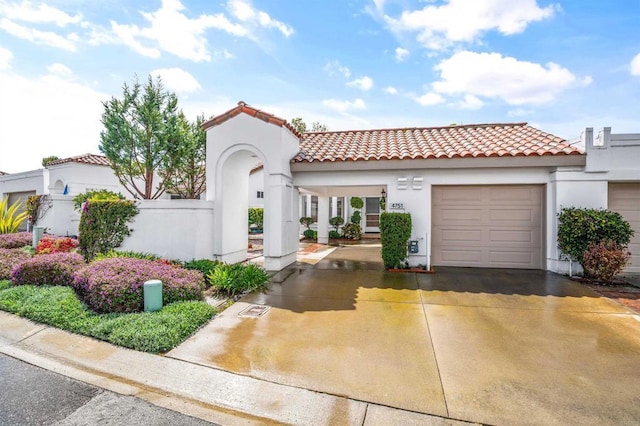 mediterranean / spanish-style home with stucco siding, driveway, a tile roof, fence, and a garage