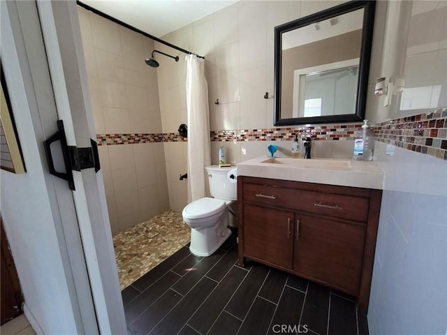 bathroom with vanity, a tile shower, tile walls, toilet, and tasteful backsplash