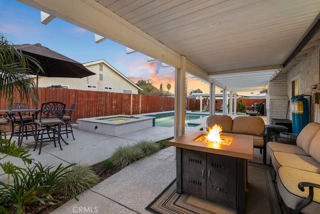 patio terrace at dusk with outdoor dining area, a fenced backyard, an outdoor living space with a fire pit, a fenced in pool, and an in ground hot tub