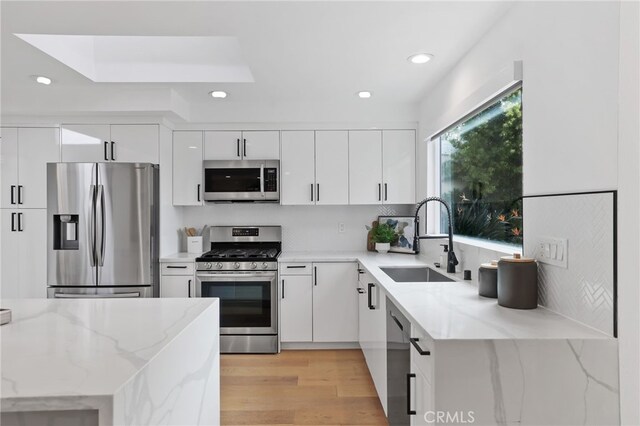 kitchen with white cabinets, stainless steel appliances, light wood-style flooring, and a sink