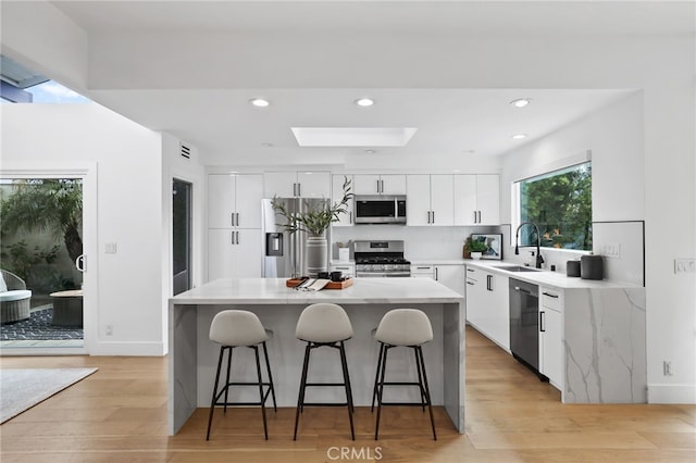 kitchen with light wood-type flooring, a sink, white cabinetry, stainless steel appliances, and a breakfast bar area