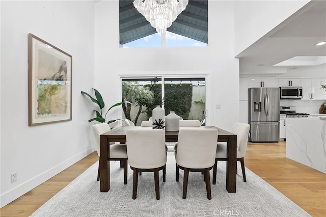 dining area with a chandelier, light wood-style flooring, high vaulted ceiling, and baseboards