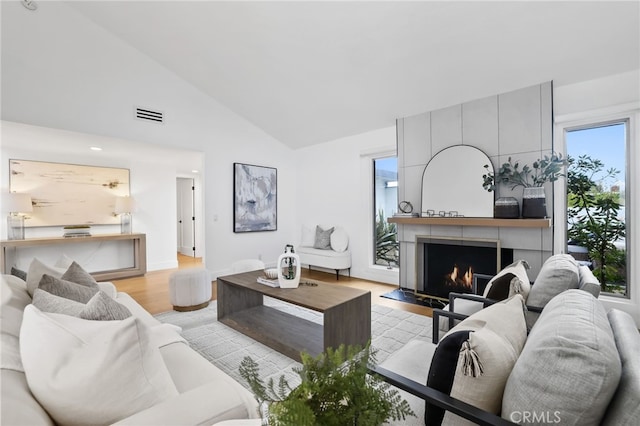 living room with baseboards, visible vents, vaulted ceiling, light wood-type flooring, and a large fireplace