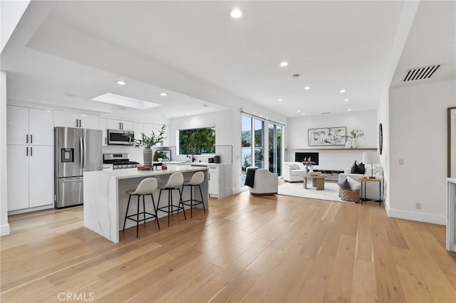 kitchen featuring a center island, a kitchen bar, light wood-type flooring, appliances with stainless steel finishes, and white cabinets