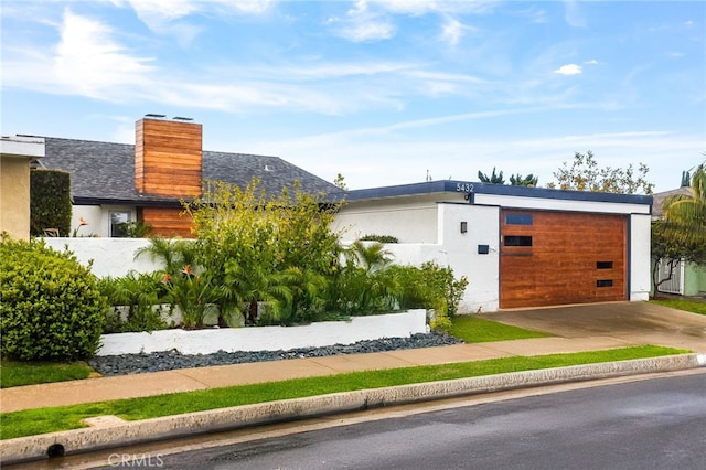 view of front of property featuring stucco siding, a garage, a chimney, and driveway