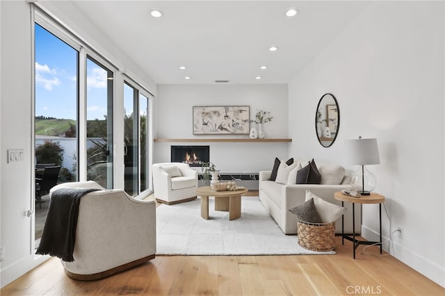 living area featuring recessed lighting, wood finished floors, baseboards, and a warm lit fireplace