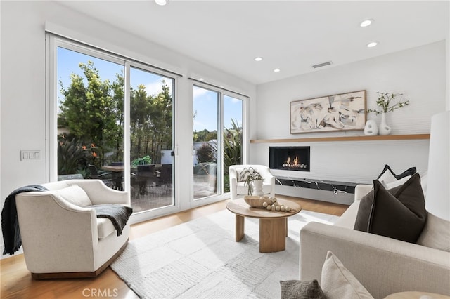 living room with visible vents, recessed lighting, a warm lit fireplace, and wood finished floors