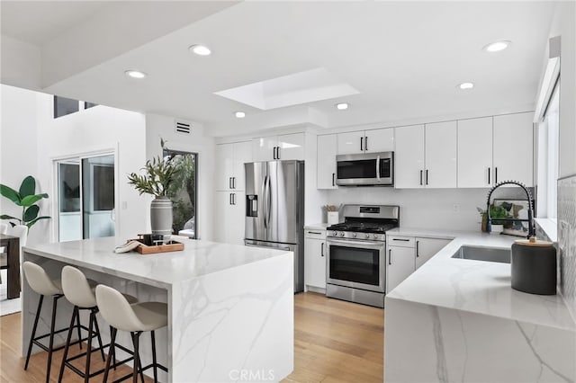 kitchen featuring a skylight, a sink, stainless steel appliances, light wood-style floors, and a kitchen bar