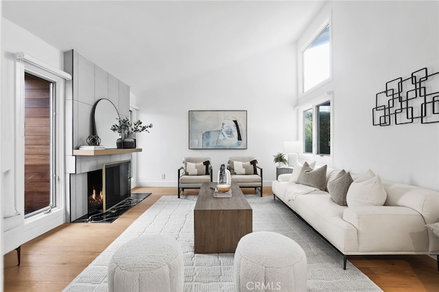 living area featuring light wood-style flooring, high vaulted ceiling, and a large fireplace