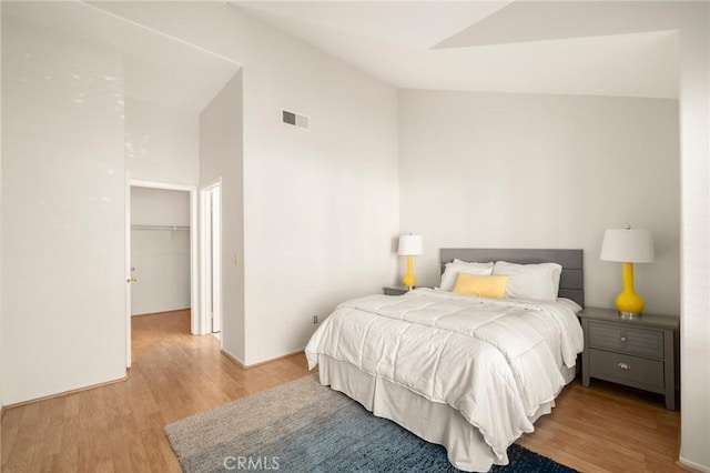 bedroom featuring visible vents, lofted ceiling, a walk in closet, and light wood-style flooring