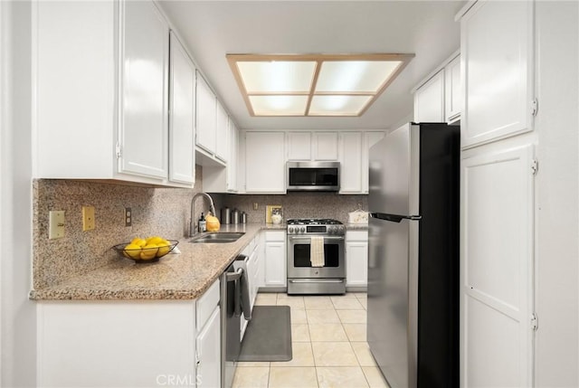 kitchen with a sink, backsplash, white cabinetry, appliances with stainless steel finishes, and light tile patterned floors