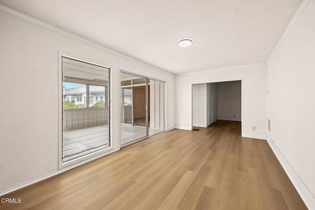 empty room featuring visible vents, wood finished floors, baseboards, and ornamental molding