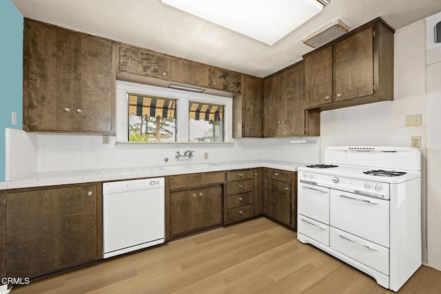 kitchen featuring visible vents, a sink, white appliances, light wood-style floors, and dark brown cabinets