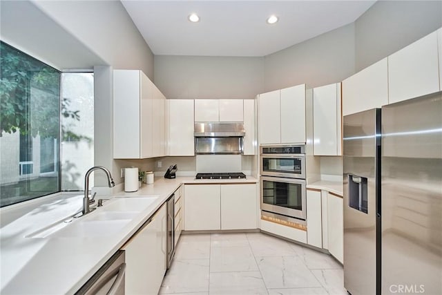 kitchen featuring under cabinet range hood, light countertops, stainless steel appliances, marble finish floor, and white cabinetry