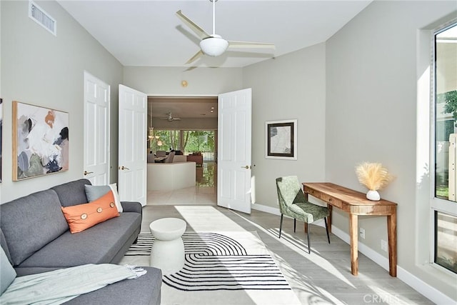 living room with visible vents, baseboards, ceiling fan, and light wood finished floors