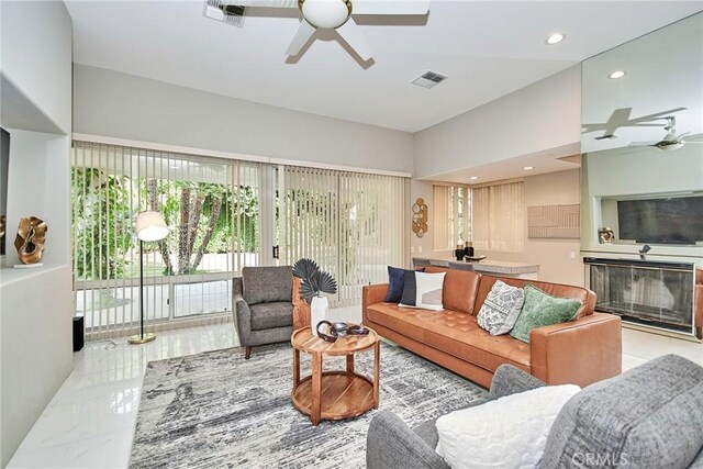 living area with recessed lighting, visible vents, a glass covered fireplace, and ceiling fan