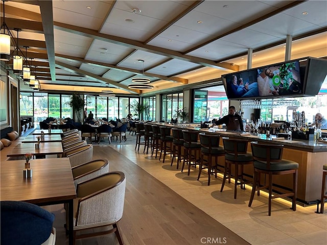 bar with wood finished floors, vaulted ceiling with beams, and a community bar