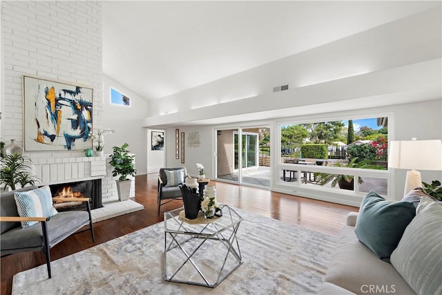 living area featuring visible vents, a brick fireplace, high vaulted ceiling, and wood finished floors