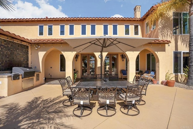 rear view of house with exterior kitchen, outdoor dining space, a patio, and stucco siding