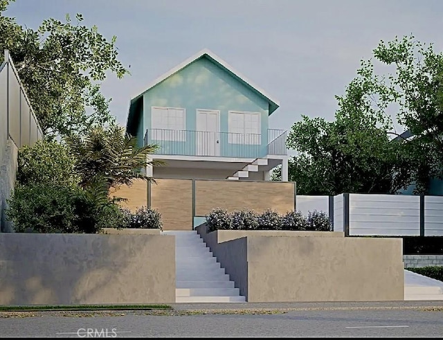 view of front of property with stairway, a balcony, a fenced front yard, and stucco siding