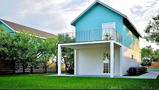 back of house featuring stucco siding, a balcony, a yard, and fence