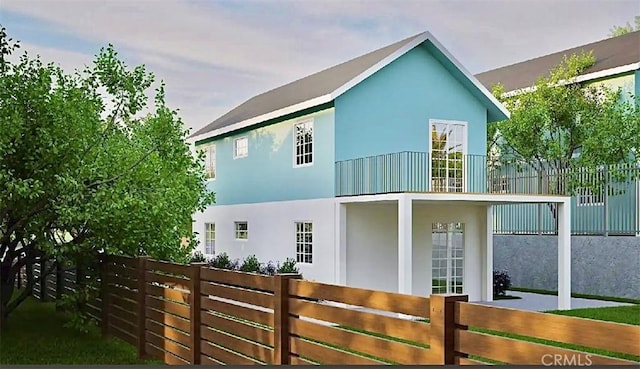 rear view of property featuring a balcony, a fenced front yard, and stucco siding