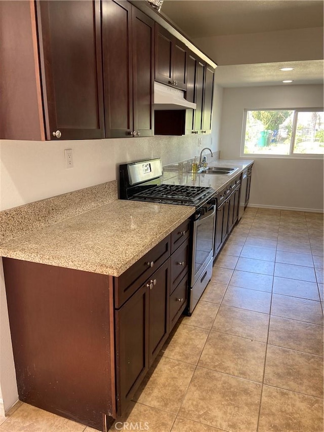 kitchen featuring stainless steel gas range oven, dark brown cabinetry, under cabinet range hood, light tile patterned floors, and a sink