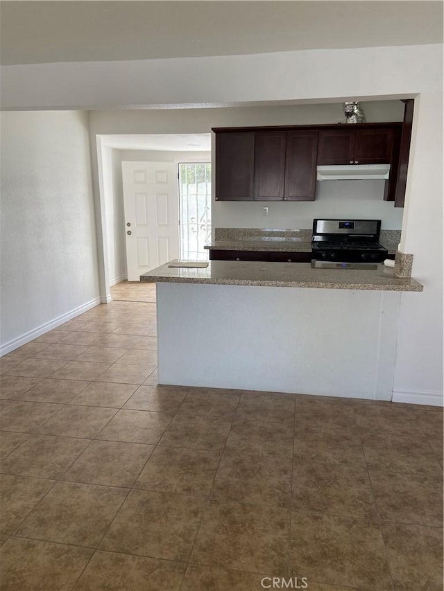 kitchen with baseboards, stainless steel range with gas stovetop, stone countertops, dark brown cabinetry, and under cabinet range hood