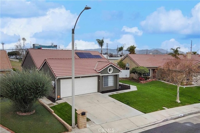 view of front facade featuring a front lawn, a tile roof, roof mounted solar panels, a garage, and driveway