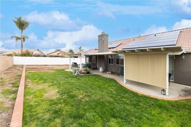 back of house with solar panels, a patio, a lawn, and a fenced backyard