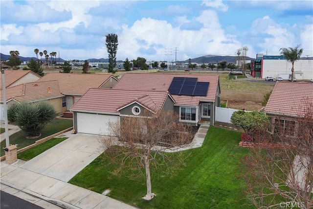 ranch-style home with a front yard, fence, driveway, solar panels, and a tiled roof