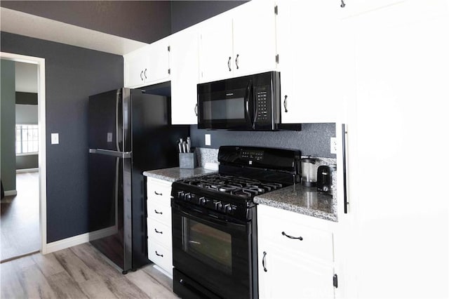 kitchen featuring black appliances, dark stone countertops, white cabinets, light wood finished floors, and baseboards