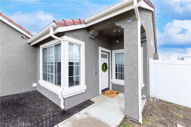 property entrance featuring stucco siding, a tile roof, and fence