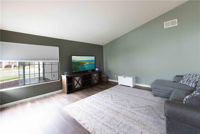 living room featuring visible vents, lofted ceiling, baseboards, and wood finished floors