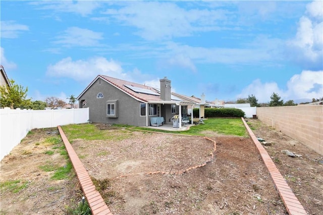 back of property with stucco siding, roof mounted solar panels, a patio, a fenced backyard, and a yard