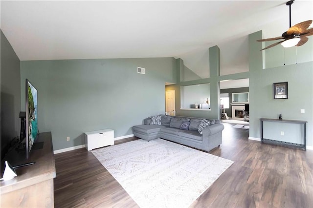 living room featuring visible vents, high vaulted ceiling, a fireplace with raised hearth, wood finished floors, and baseboards