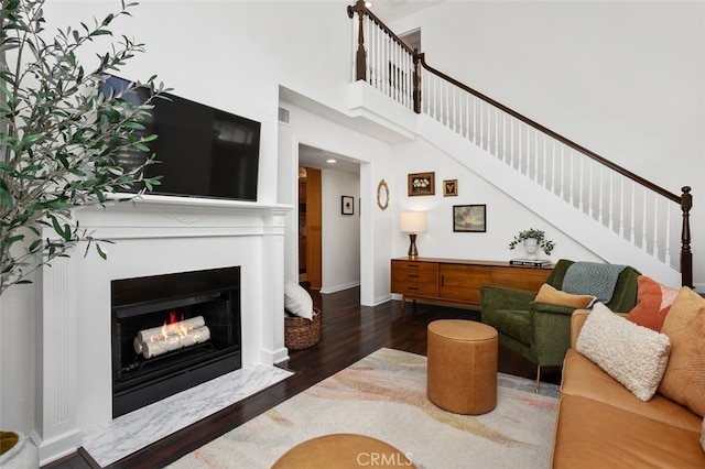 living room featuring baseboards, a fireplace with flush hearth, stairs, a towering ceiling, and wood finished floors