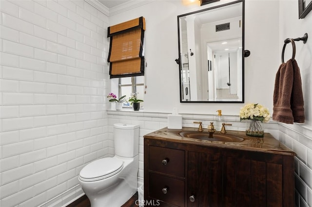 half bathroom featuring visible vents, toilet, tile walls, crown molding, and vanity