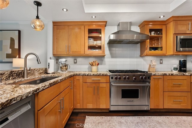 kitchen with light stone counters, a sink, stainless steel appliances, wall chimney exhaust hood, and backsplash