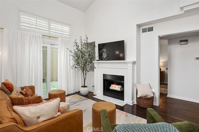 living area with visible vents, baseboards, a fireplace with flush hearth, and hardwood / wood-style floors