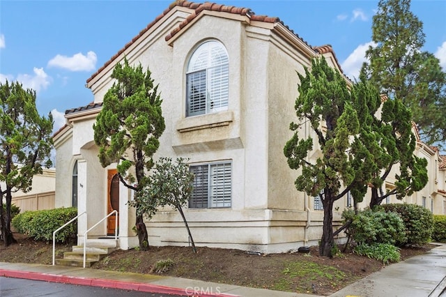 mediterranean / spanish-style house featuring stucco siding, entry steps, a tile roof, and fence